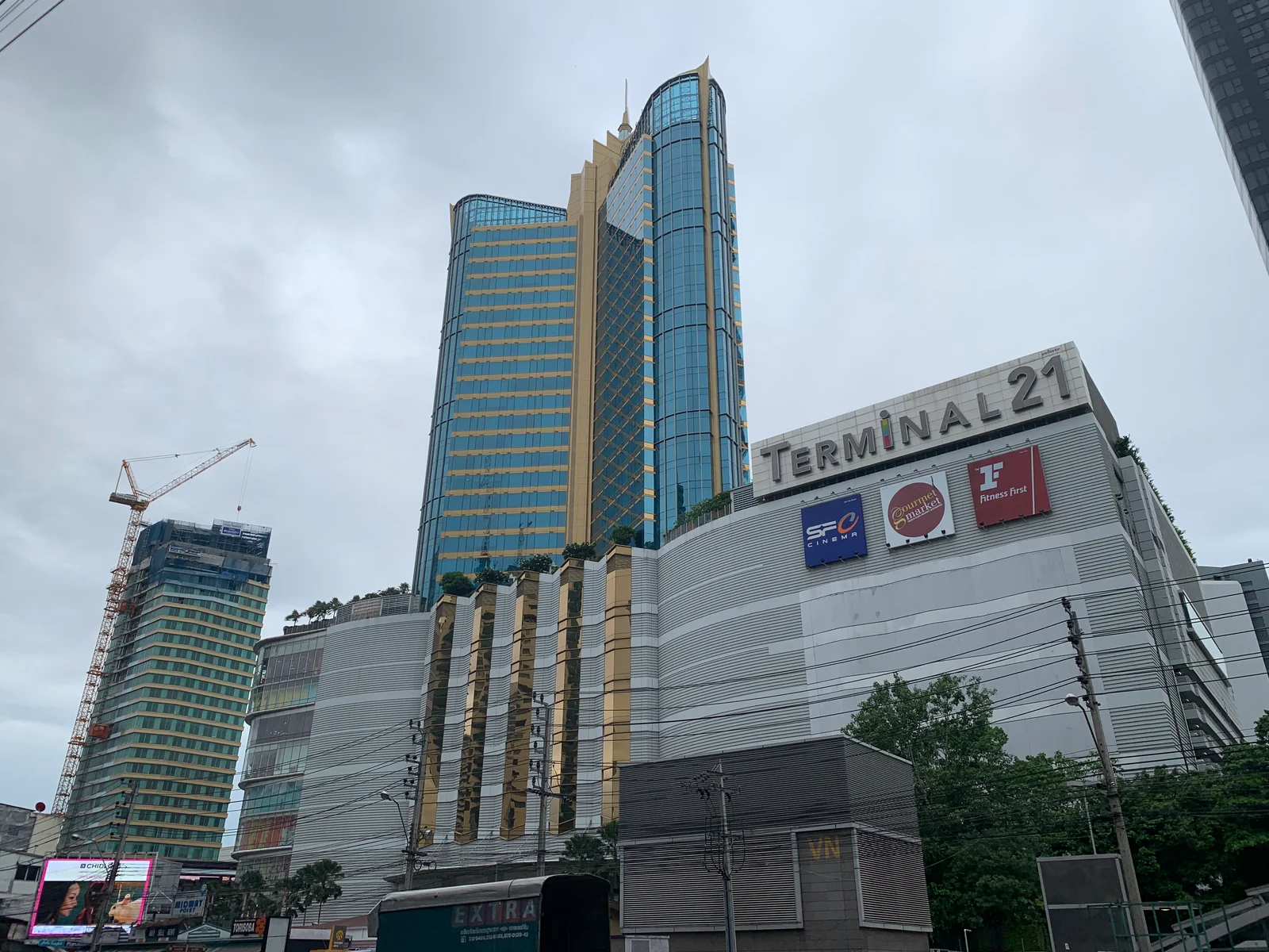 TERMINAL 21 간판이 붙은 쇼핑몰 건물 위로 솟은 푸른 유리 외벽 타워와 왼쪽의 공사 크레인